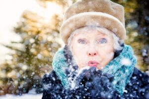 Close-up of a senior woman blowing snow to camera Shot in Canadian forest at sunset.