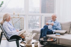 two older persons sit on couch and talk