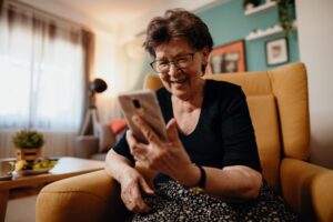 Elderly woman smiling whilst looking at a phone.