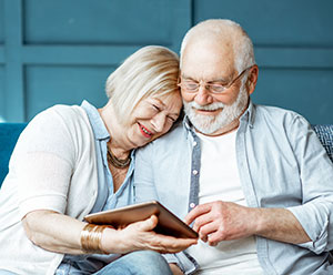 Lovely senior couple dressed casually using digital tablet while sitting together on the comfortable couch at home